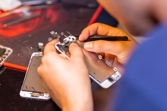 A man is repairing a mobile phone. In the frame, his hands and details of the device. repair shop for gadgets